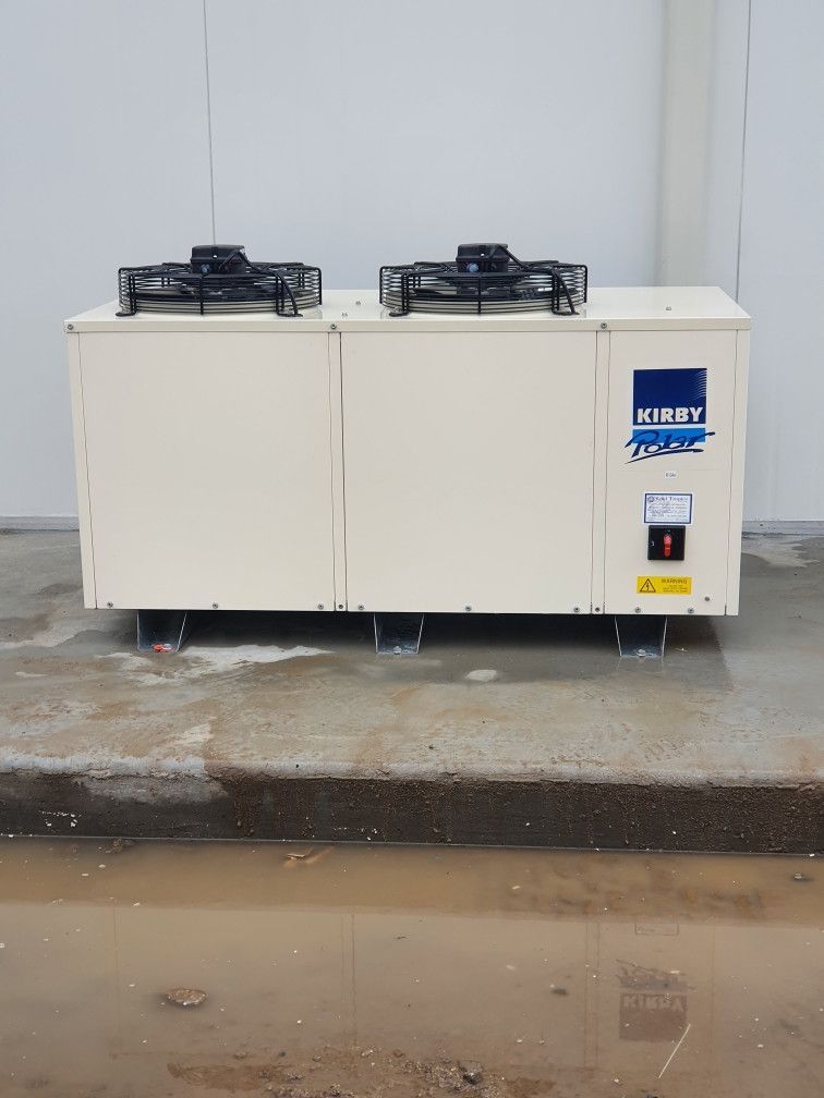Cream-colored industrial air conditioning unit with two top fans, set on concrete floor, near a white wall.— Cool Tropics Air Conditioning & Refrigeration in Mourilyan Harbour, QLD