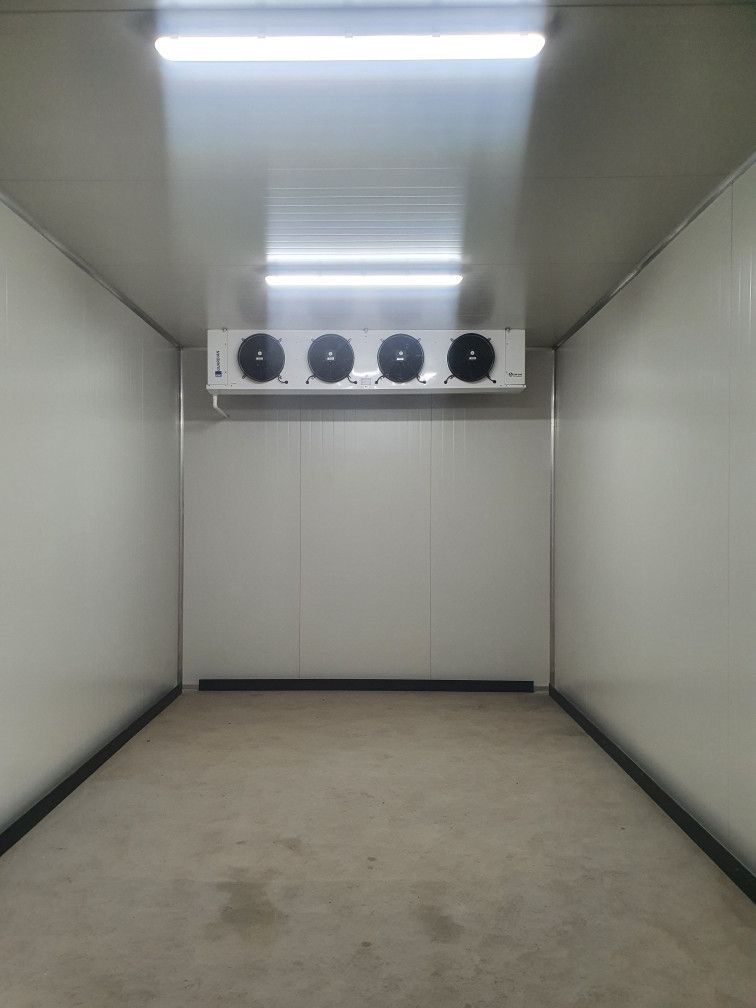 Empty walk-in freezer with white walls, ceiling, and floor. Overhead cooler unit with four fans.— Cool Tropics Air Conditioning & Refrigeration in Cardwell, QLD