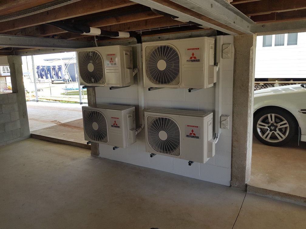Four Mitsubishi air conditioning units mounted on a wall beneath a house, next to a car.— Cool Tropics Air Conditioning & Refrigeration in Mourilyan Harbour, QLD