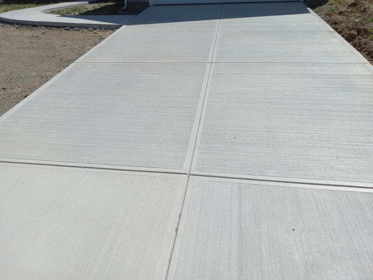 Gray concrete driveway with expansion joints, leading to a garage door.
