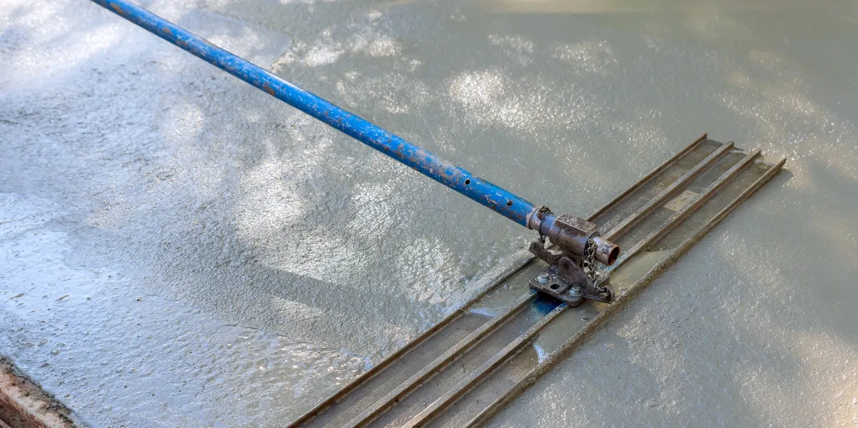 A concrete worker smoothing wet concrete with a large, blue-handled float tool.