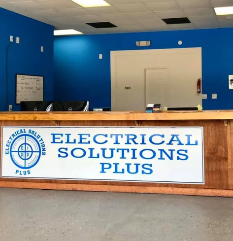 Reception area of Electrical Solutions Plus, blue walls, wooden desk with company logo.