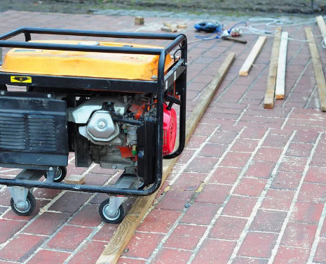 A generator on wheels sits on a brick surface next to wooden planks.