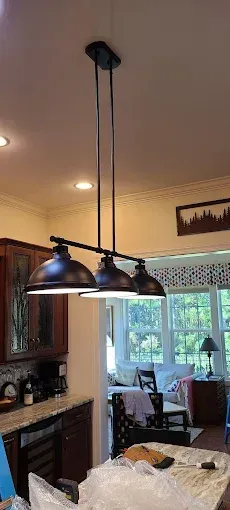 A dark metal, three-light pendant lamp hangs over a kitchen island. The lamp is on, illuminating the space.