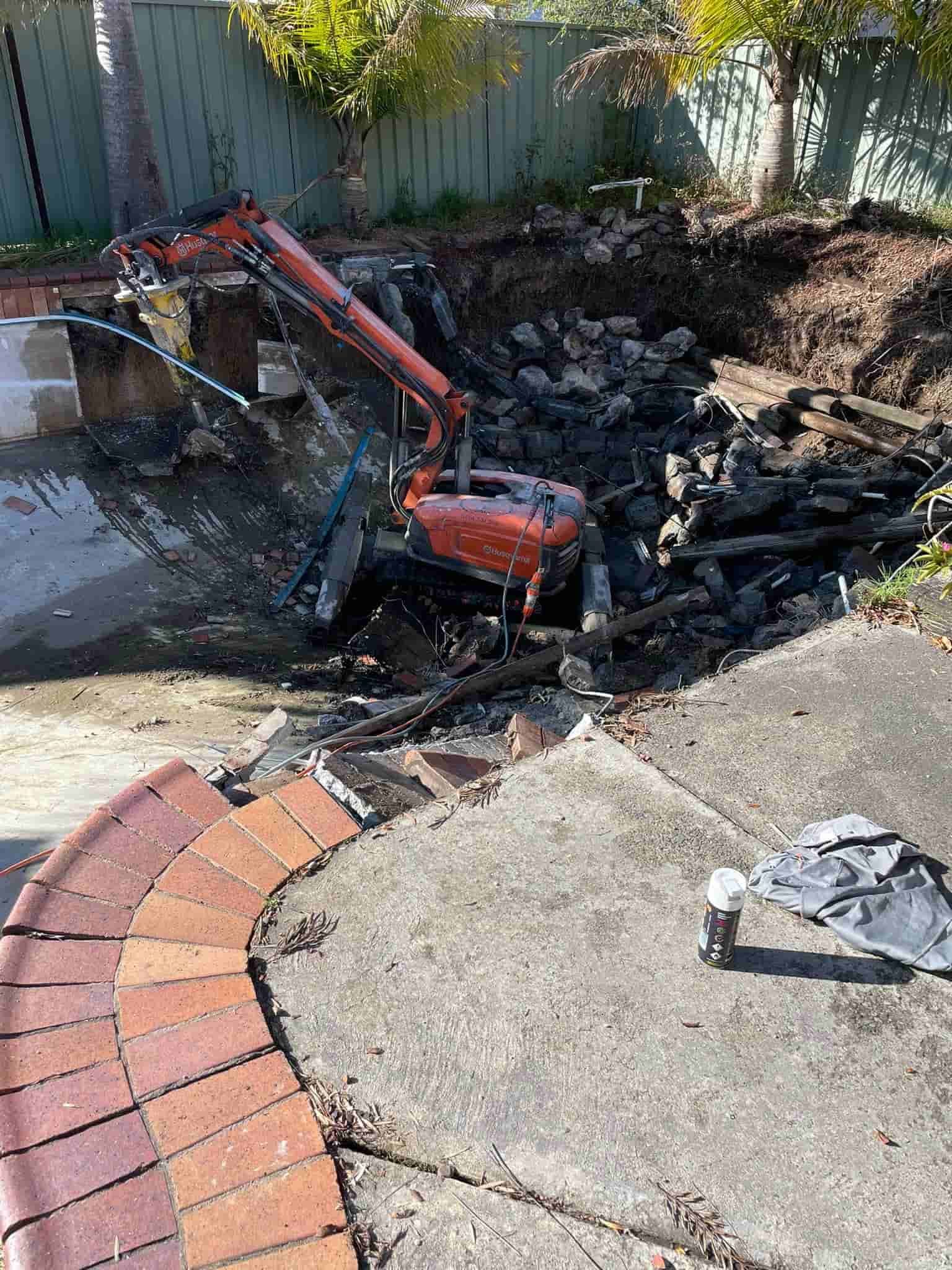 A small excavator is digging a hole in the ground in a backyard. — Newcastle Cut N Drill Pty Ltd In Boolaroo, NSW