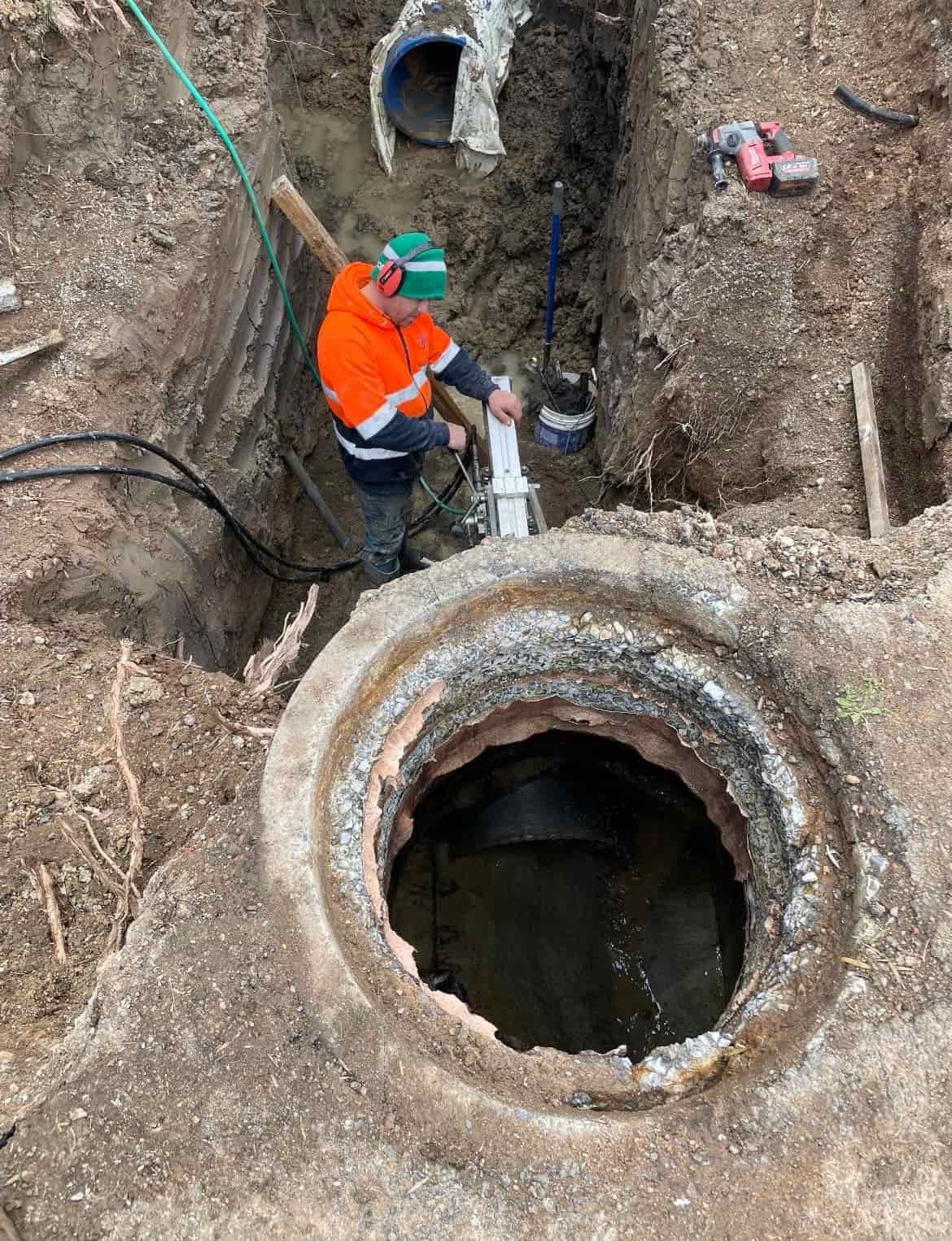 A man is working on a pipe in a hole in the ground. — Newcastle Cut N Drill Pty Ltd In Boolaroo, NSW