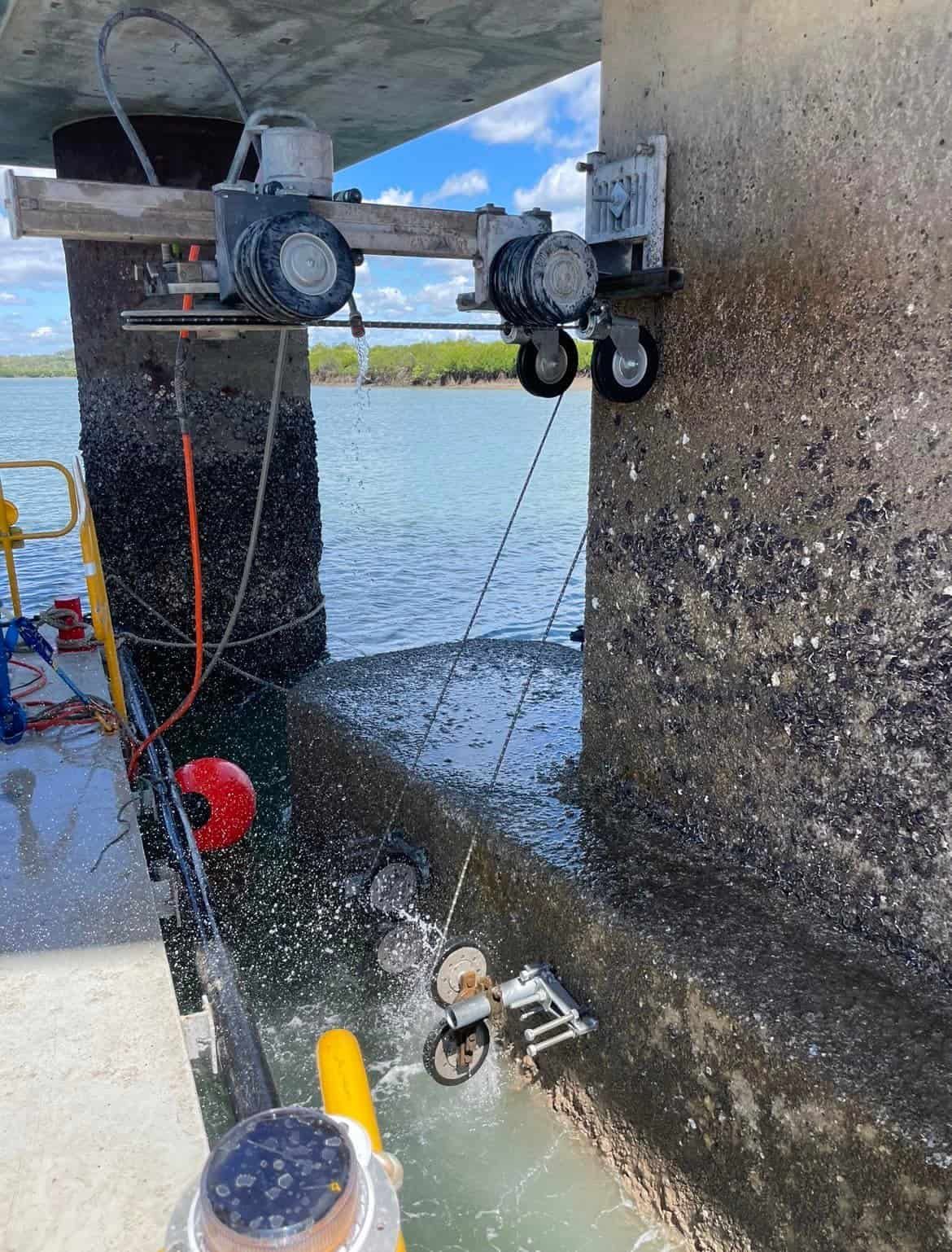 A machine is cutting concrete under a bridge over a body of water. — Newcastle Cut N Drill Pty Ltd In Boolaroo, NSW