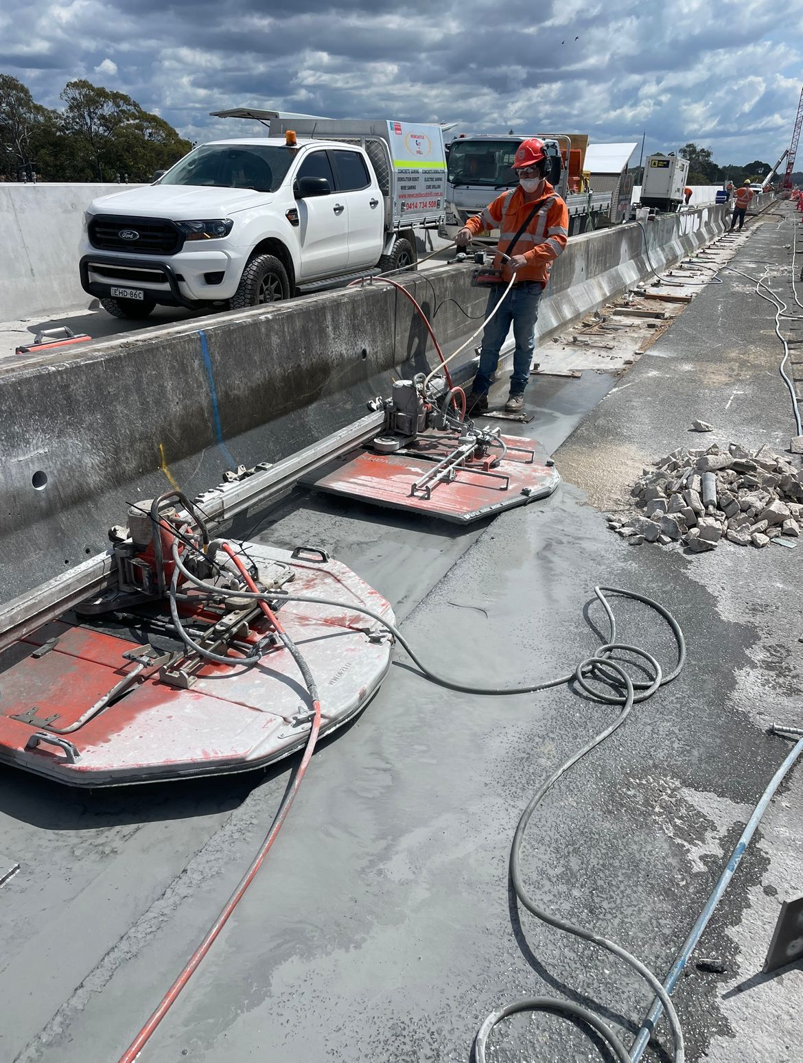 A man is using a Machine Is Cutting A Piece of concrete on the side of a road barrier— Newcastle Cut N Drill Pty Ltd In Boolaroo, NSW