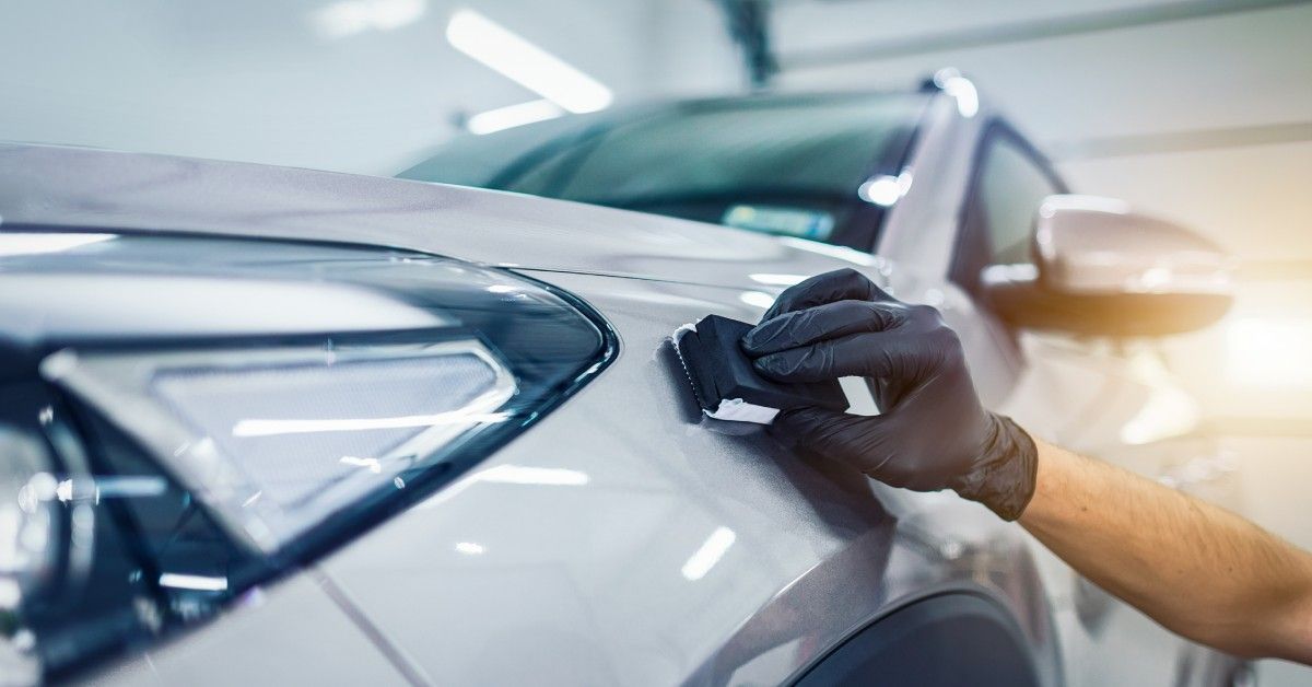 Close-up of a hand wearing a black rubber glove applying a ceramic coating to a silver vehicle.