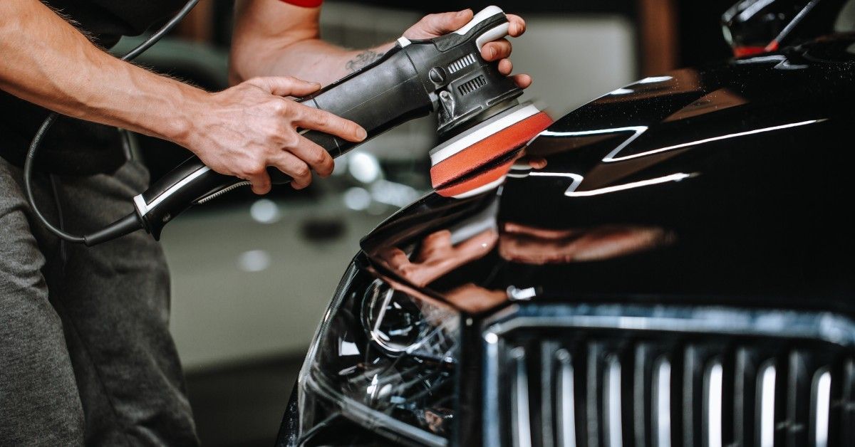 Closeup of a man holding an orbital polishing tool as he details the exterior of a black vehicle.