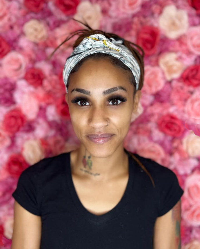A woman wearing a headband stands in front of a wall of pink roses