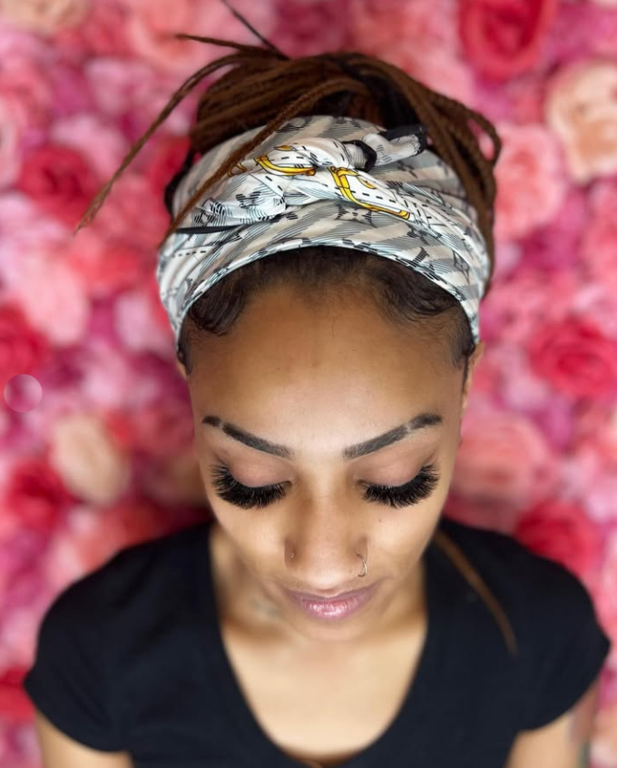 A woman wearing a headband is standing in front of a wall of pink flowers.