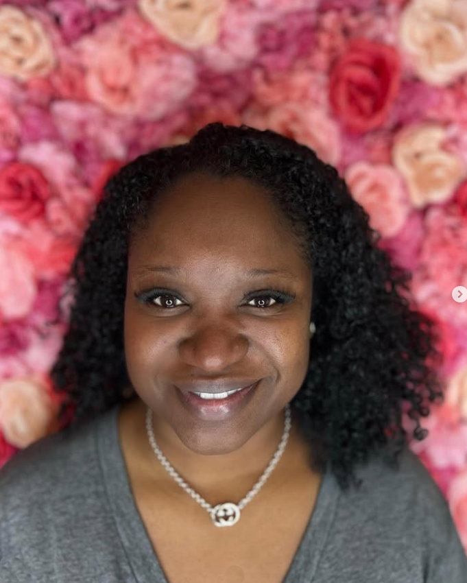 A woman is smiling in front of a wall of pink roses
