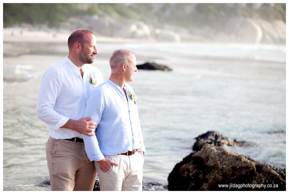 Two men are standing on a beach looking at the ocean.
