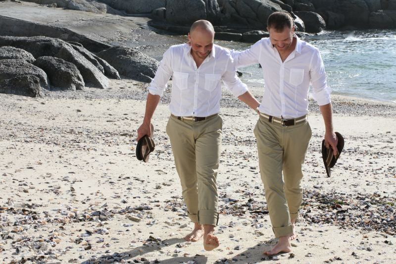 Two men are walking on the beach holding hands
