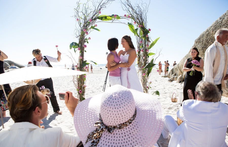 A bride and groom are kissing on a rocky beach.