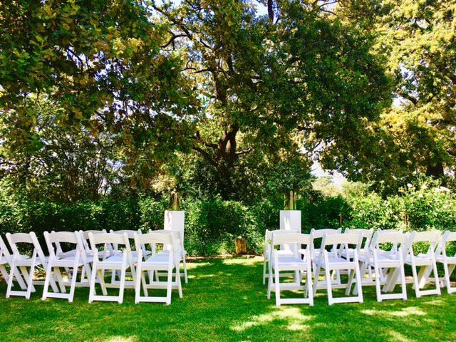 A row of white folding chairs are lined up in a grassy field.
