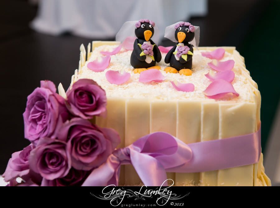 A wedding cake with two penguins on top and purple roses