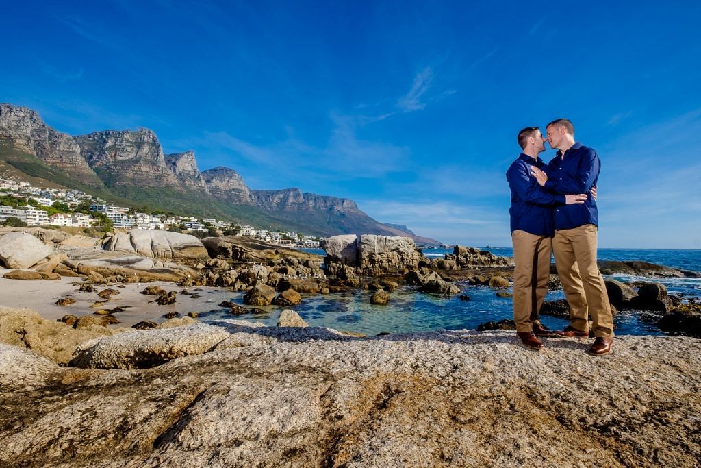 Two men are standing next to each other on a rocky beach.