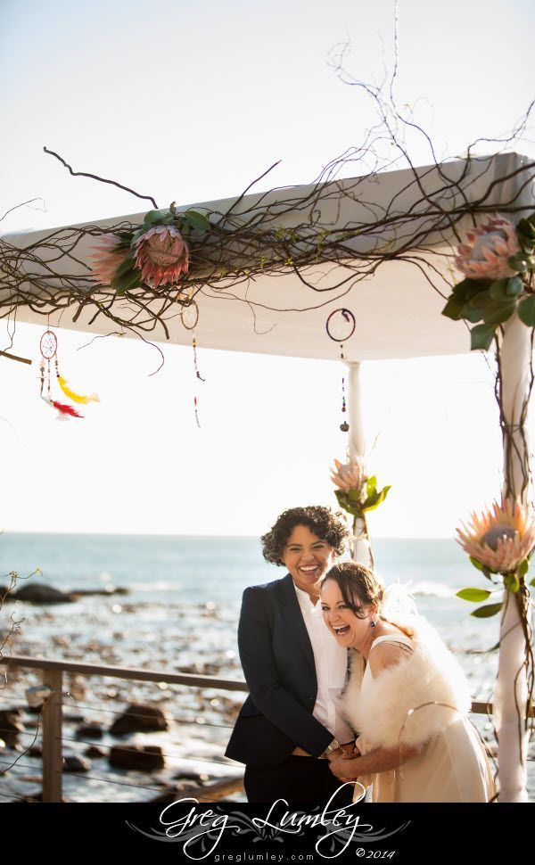 A bride and groom are posing for a picture in front of the ocean.