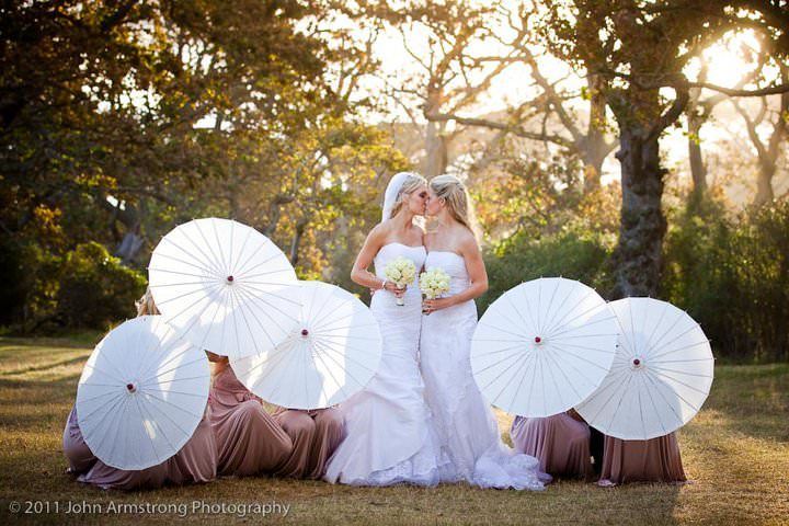 A bride and her bridesmaids are posing for a picture with white umbrellas.