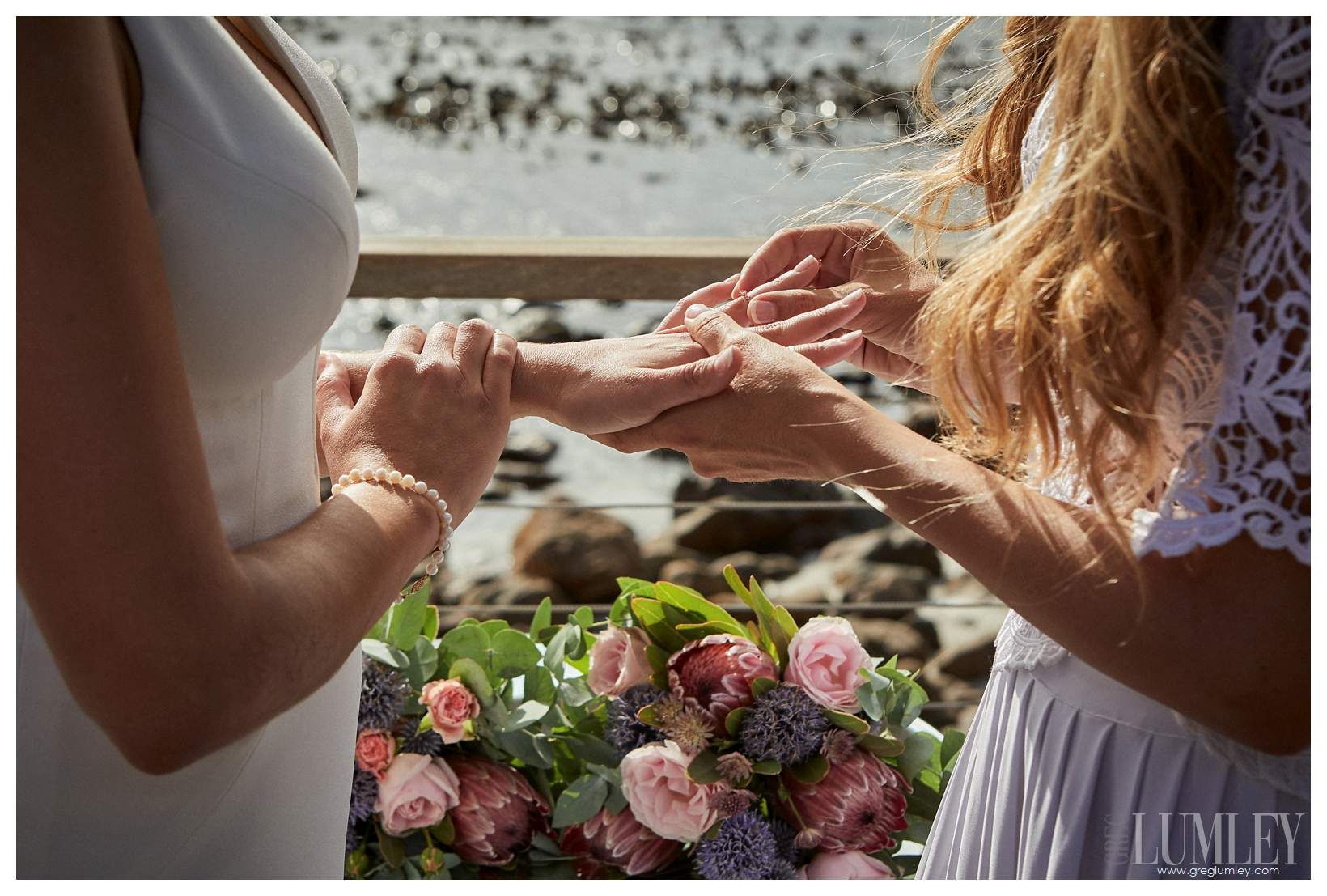 Two women are holding hands and putting rings on each other 's fingers.