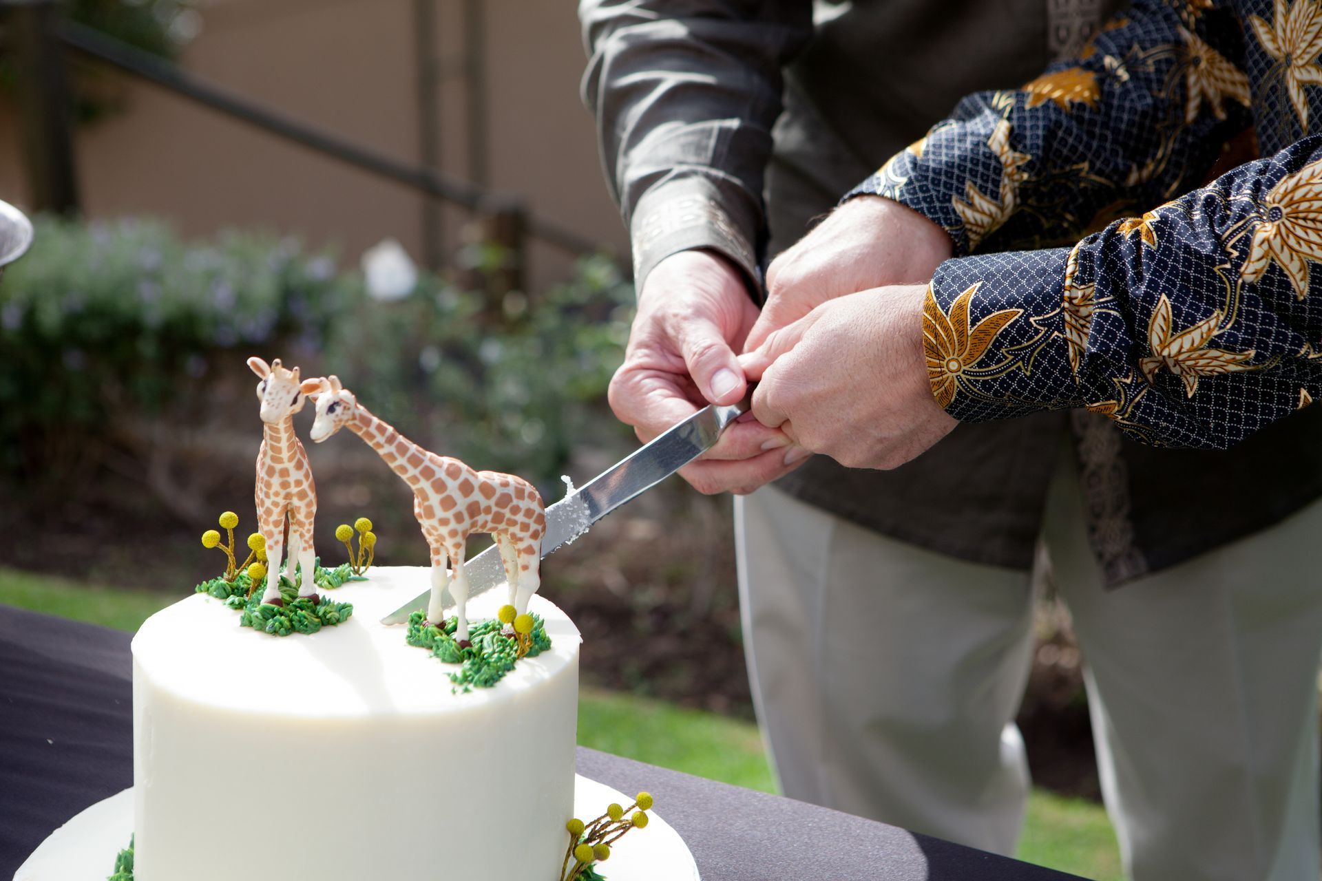 Two people are cutting a cake with giraffes on it
