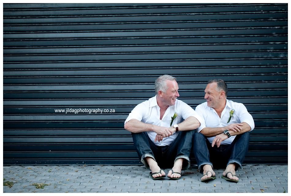Two men are sitting next to each other in front of a black garage door.