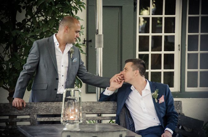 A man in a suit is kissing another man 's hand while sitting on a bench.