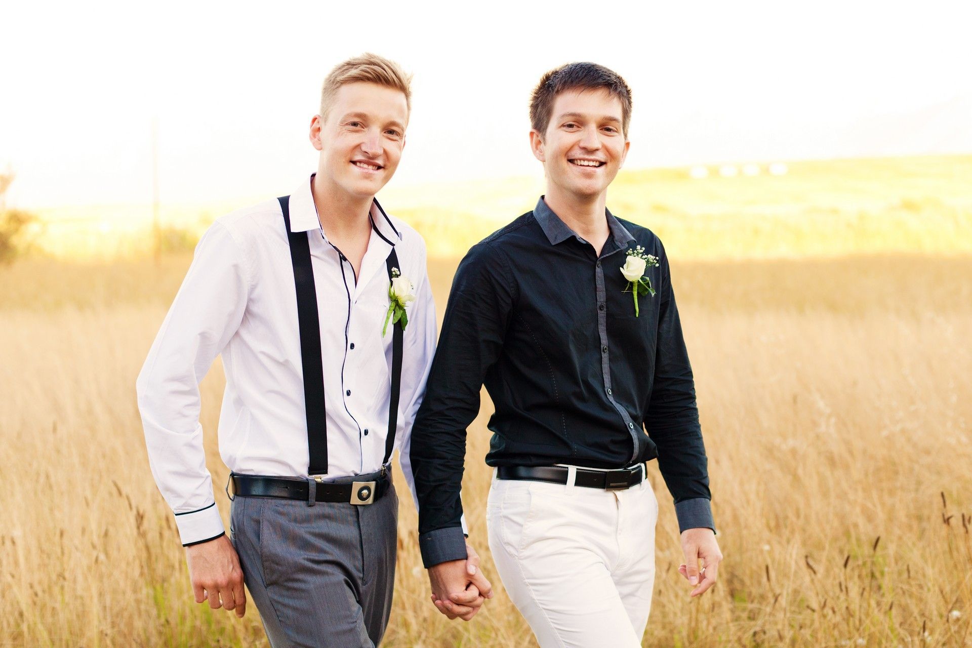 Two men are holding hands while walking through a field.