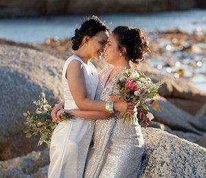 Two women are hugging each other on a rock near the water.