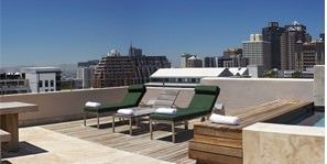 A rooftop deck with chairs and a table with a view of the city.
