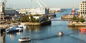 Boats are docked in a harbor with a lighthouse in the background.