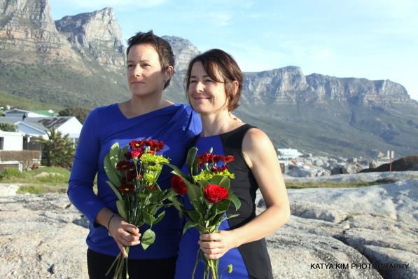 Two women standing next to each other holding flowers in front of a mountain