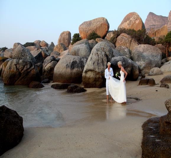 A bride and groom standing on a rocky beach