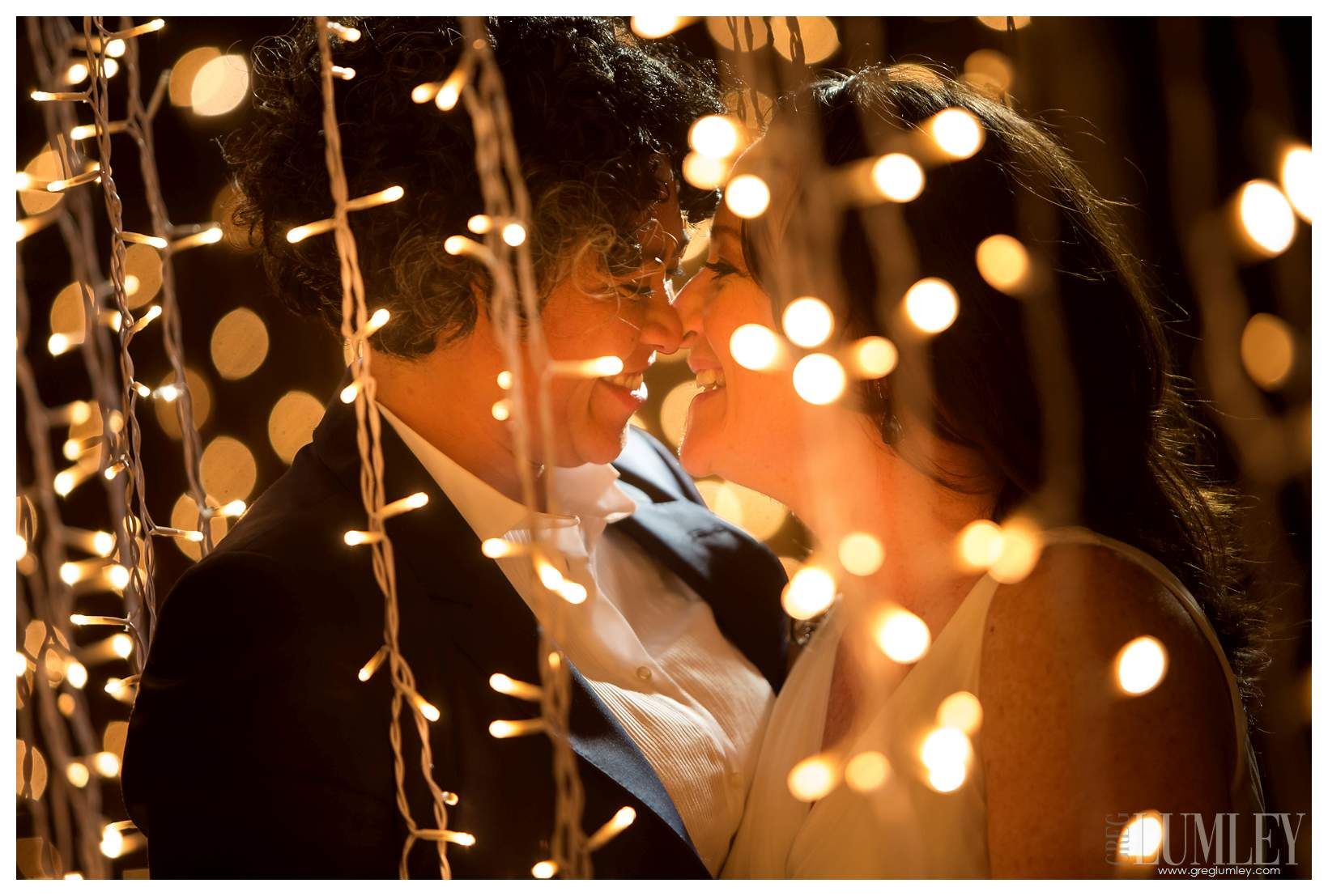 A bride and groom are kissing under a string of lights.