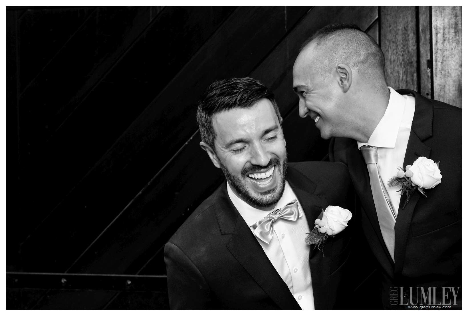 Two men in suits and bow ties are laughing together in a black and white photo.