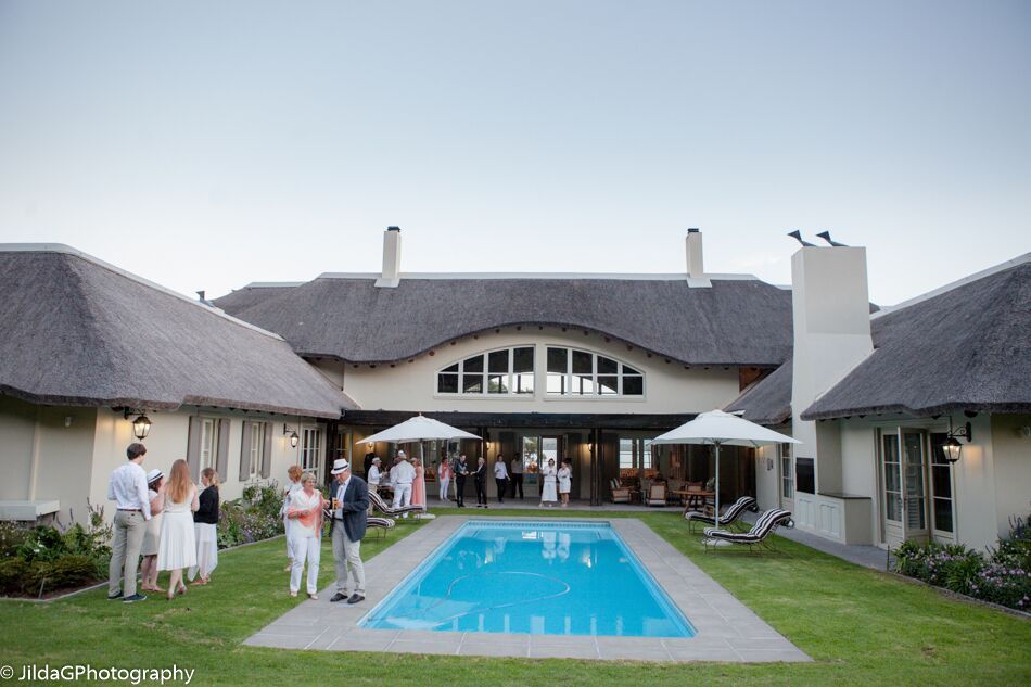 A group of people standing around a swimming pool in front of a large house
