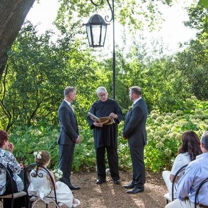 A bride and groom are holding hands during their wedding ceremony under a wooden arch.