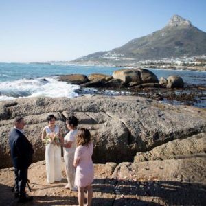A bride and groom are standing under a wooden arch on the beach.