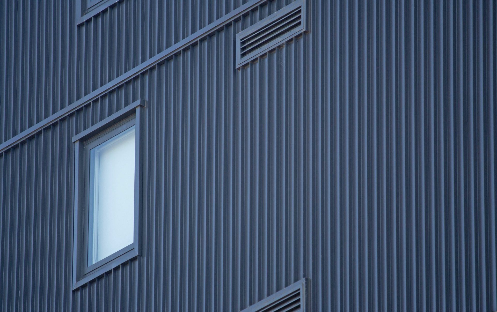 Façade de bâtiment en tôle ondulée bleu foncé avec une fenêtre et des évents.