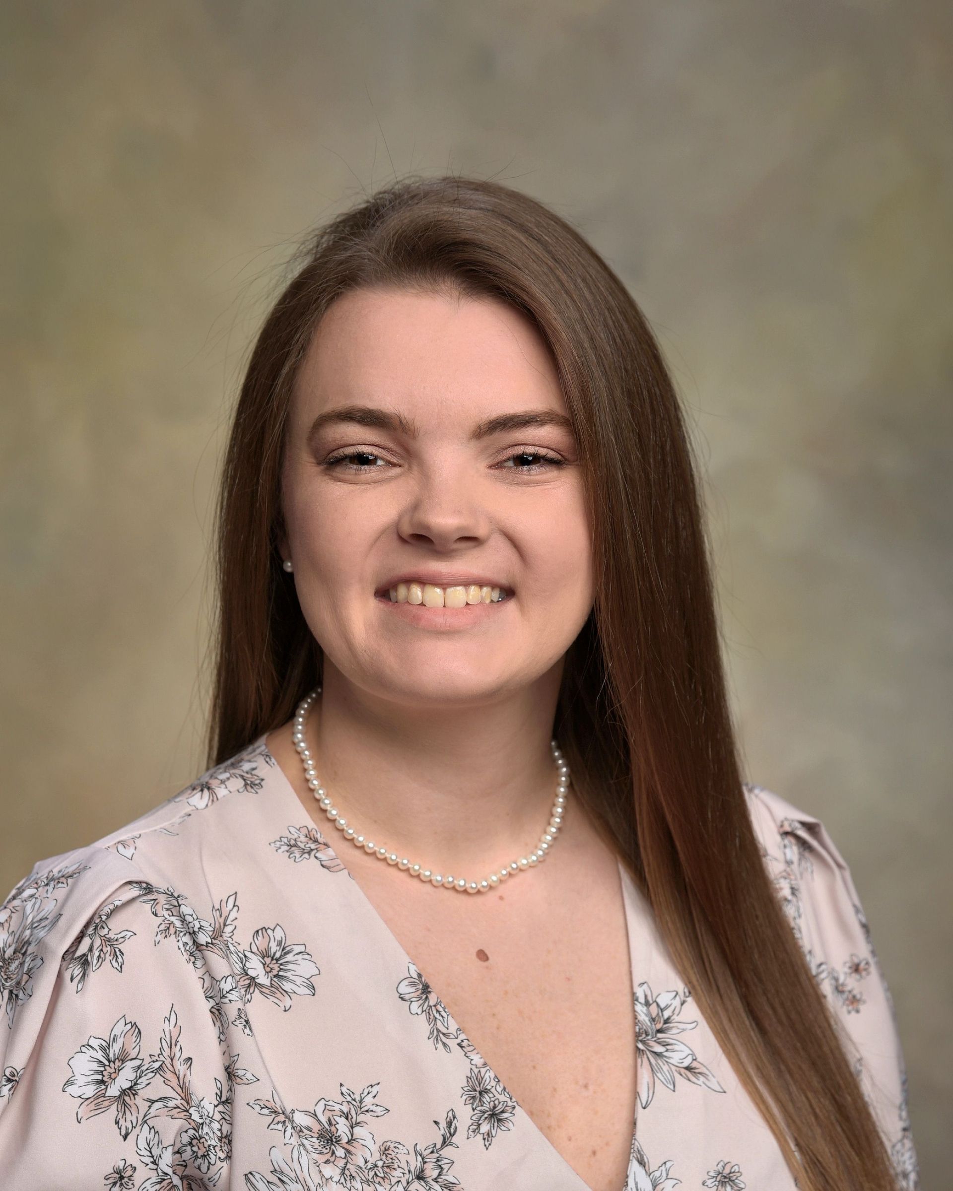 A woman in a white lab coat is smiling in front of a clock.