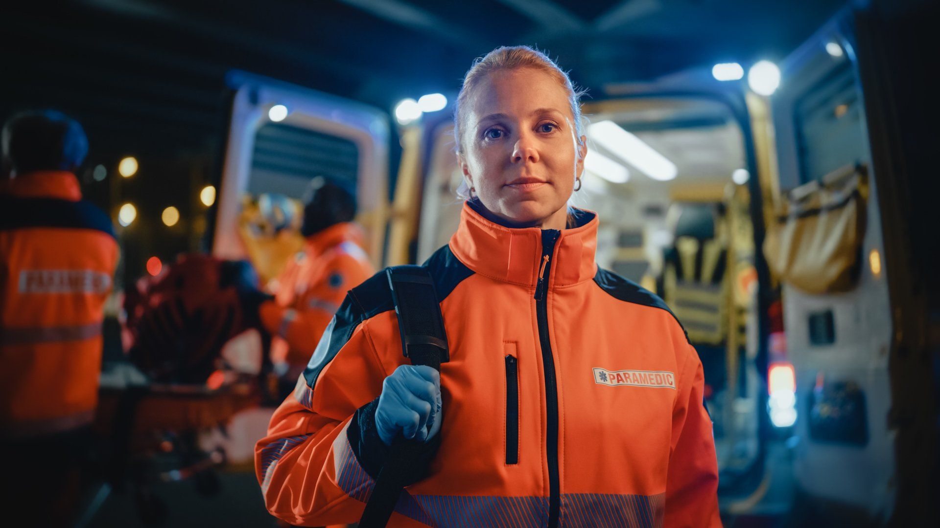 A female paramedic is standing in front of an ambulance.