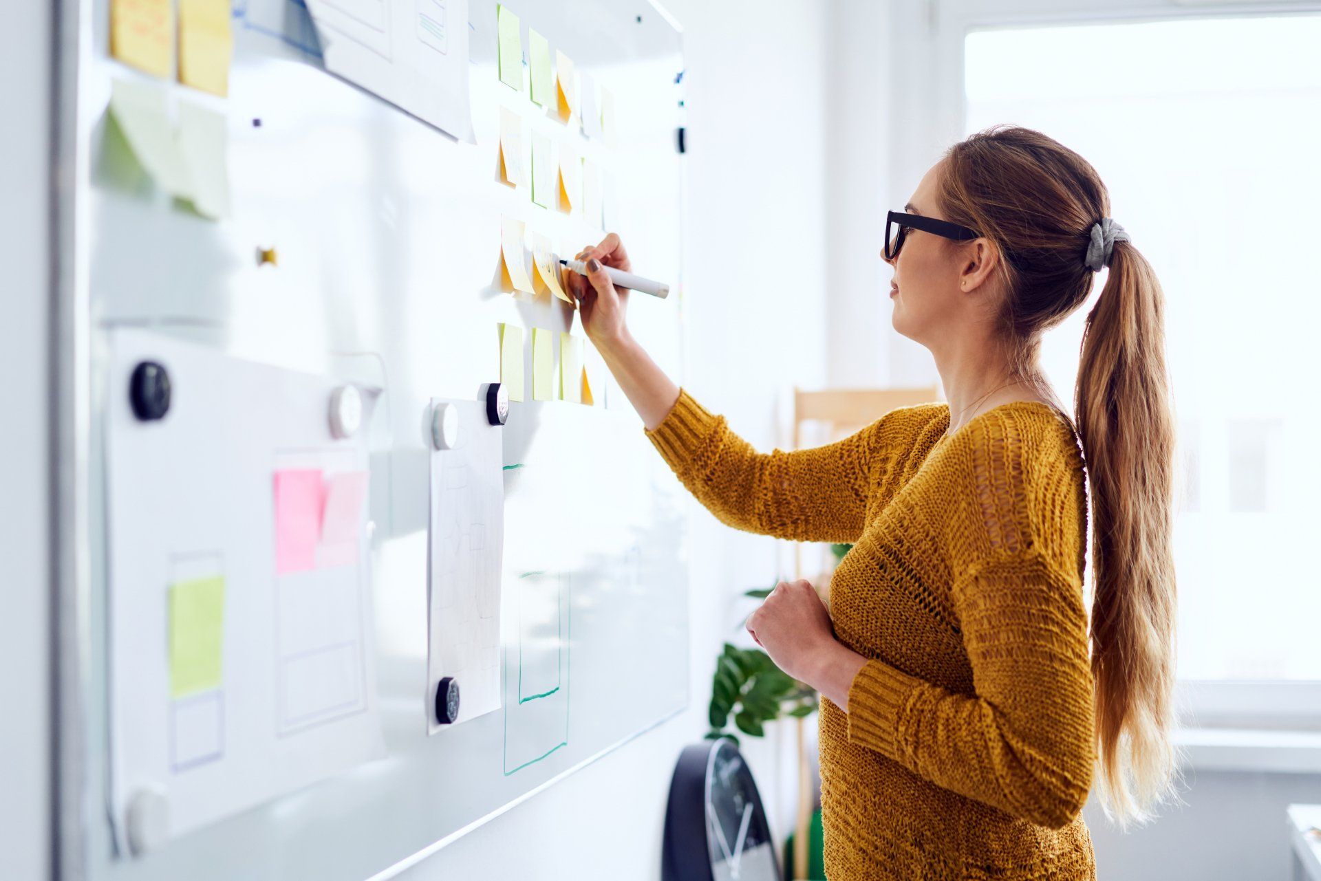 A woman is writing on a whiteboard with sticky notes.