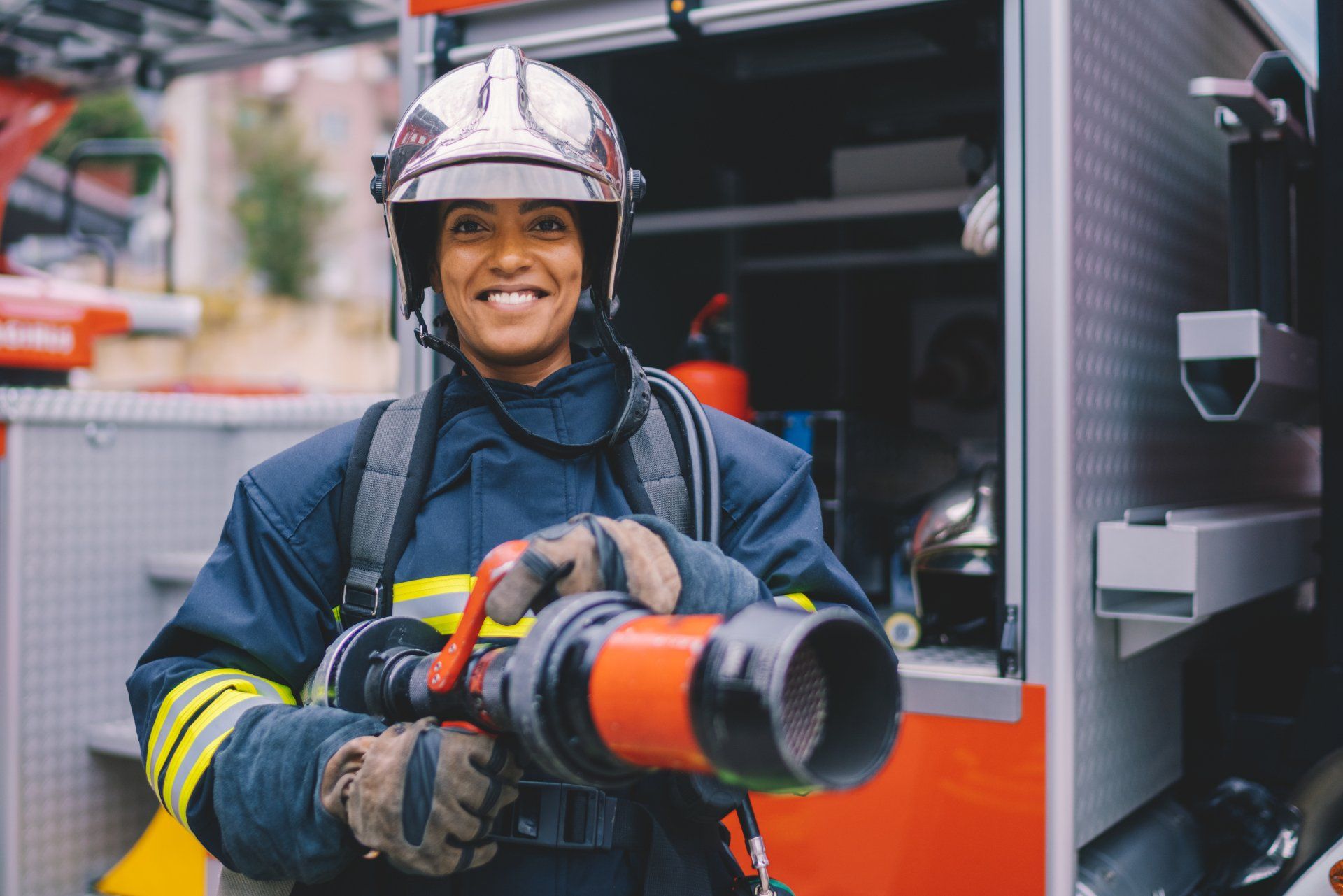 A woman firefighter is holding a fire hose in front of a fire truck.