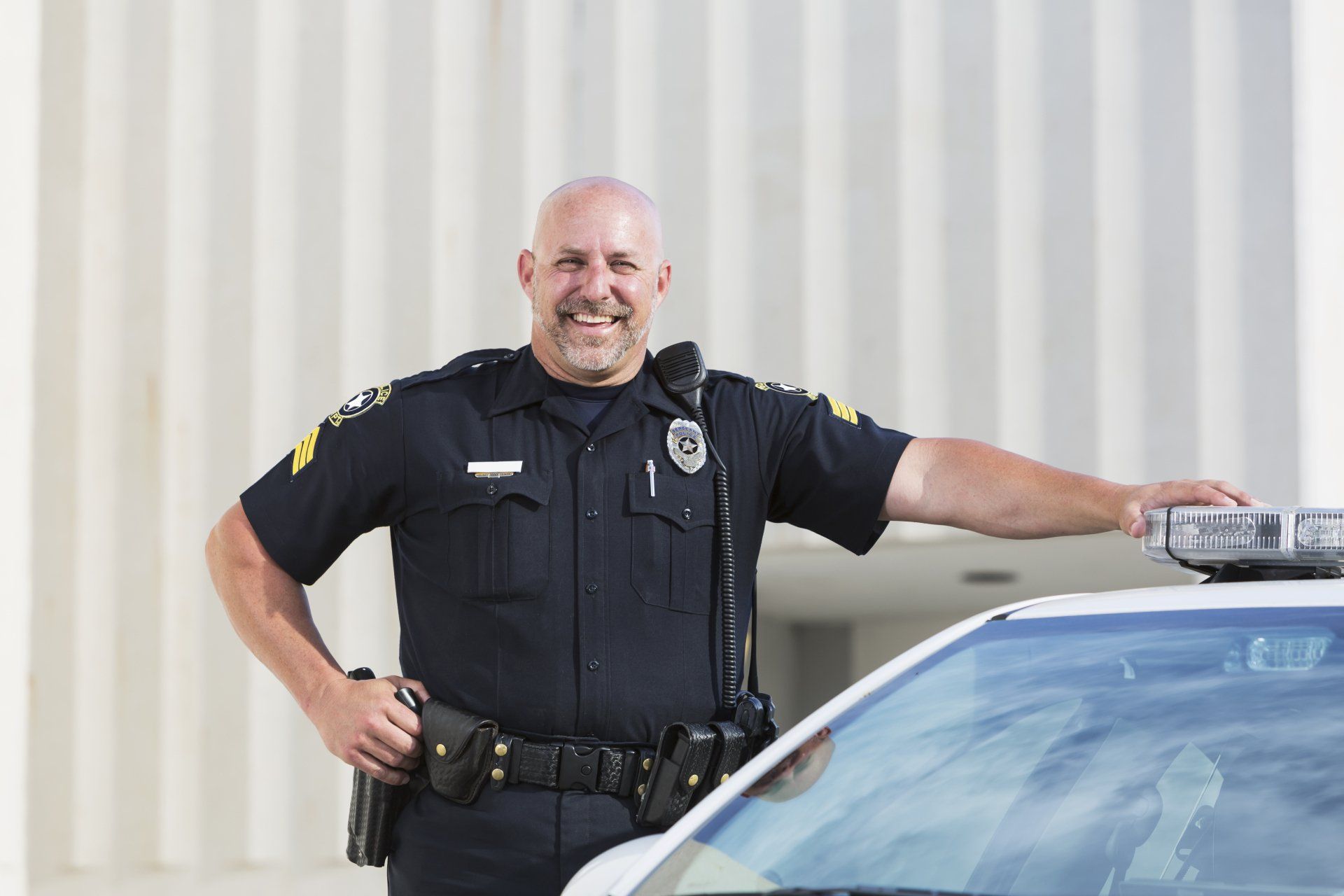 A police officer is standing next to a police car and smiling.