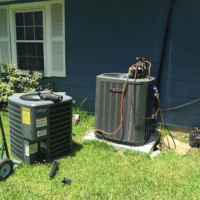 Two air conditioners are sitting in the grass in front of a blue house.