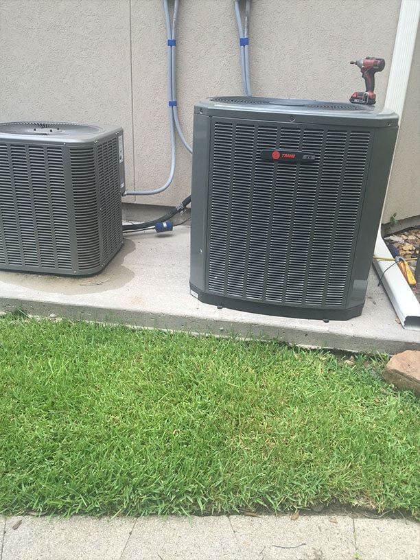 Two air conditioners are sitting next to each other on a sidewalk.