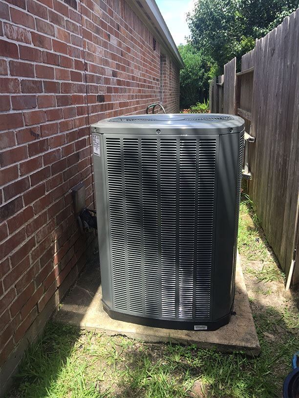 A large air conditioner is sitting outside of a brick house.