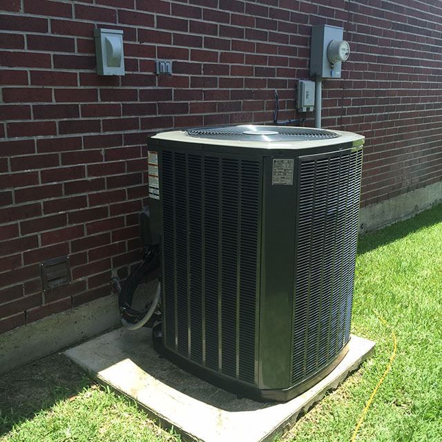 An air conditioner is sitting outside of a brick building.